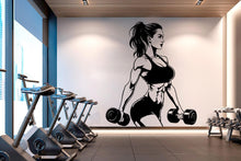 Load image into Gallery viewer, A modern gym wall decal of a strong, fit woman holding dumbbells, muscles in a bold black-and-white illustration. Set against a white wall with wood paneling, surrounded by stationary bikes and dumbbells, creating an inspiring workout space.