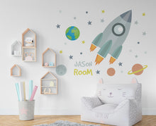 Load image into Gallery viewer, May include: A gray rocket ship with orange flames, a blue and green planet, and yellow stars on a white wall. The text "Jason Room" is written in yellow. A gray cat-shaped chair with white polka dots and the text "Cuffy Cat" is in the foreground.