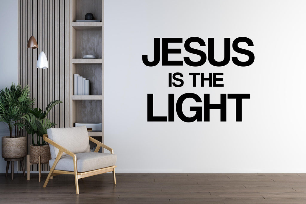 May include: A room with a white wall featuring the text "JESUS IS THE LIGHT" in bold black letters. The room includes a wooden chair, a wooden shelf with books, and potted plants. Decorative lighting hangs from the ceiling.