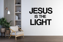 Load image into Gallery viewer, May include: A room with a white wall featuring the text "JESUS IS THE LIGHT" in bold black letters. The room includes a wooden chair, a wooden shelf with books, and potted plants. Decorative lighting hangs from the ceiling.