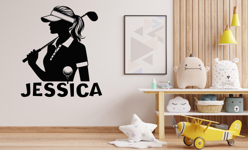 May include: Black and white silhouette of a golfer holding a golf club with the name "JESSICA" written below. The image is on a white wall with a wooden shelf and a yellow airplane toy in the background.